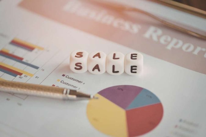 Un rapport commercial papier avec des graphiques et des dés blancs formant le mot SALE.