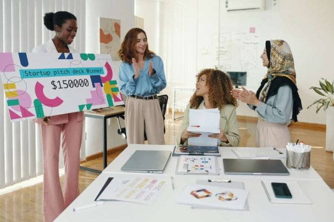 Une équipe d'entrepreneurs féminines célébrant la victoire d'un concours de pitch deck avec un gros chèque de 150 000 $.