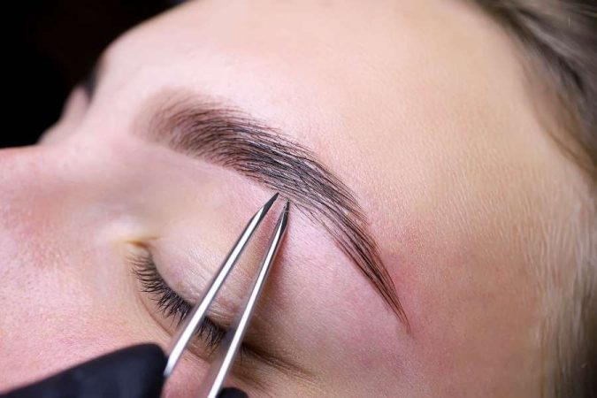 Une esthéticienne utilise une pince pour l'épilation des sourcils avec précision.